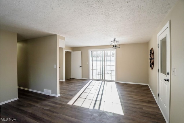 empty room featuring a textured ceiling, a chandelier, and dark hardwood / wood-style floors