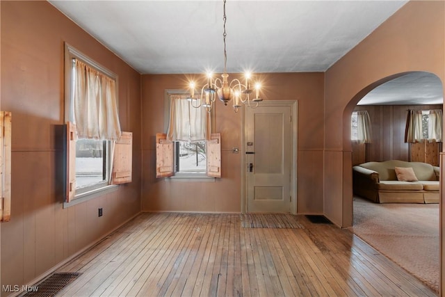 unfurnished dining area featuring light hardwood / wood-style flooring, wooden walls, and an inviting chandelier