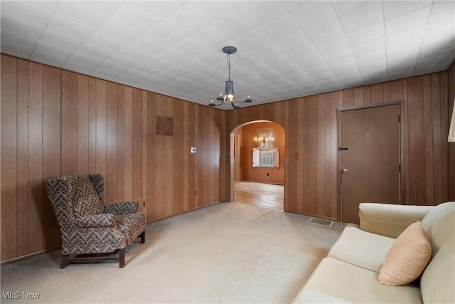 living area featuring light carpet, an inviting chandelier, and wooden walls