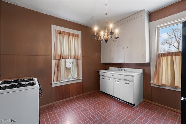 kitchen with pendant lighting, sink, white cabinetry, white range with gas cooktop, and a chandelier