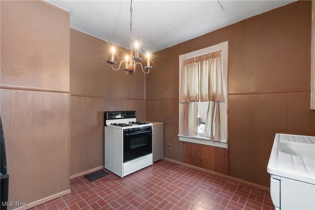 kitchen featuring decorative light fixtures, white range with gas cooktop, wooden walls, and an inviting chandelier