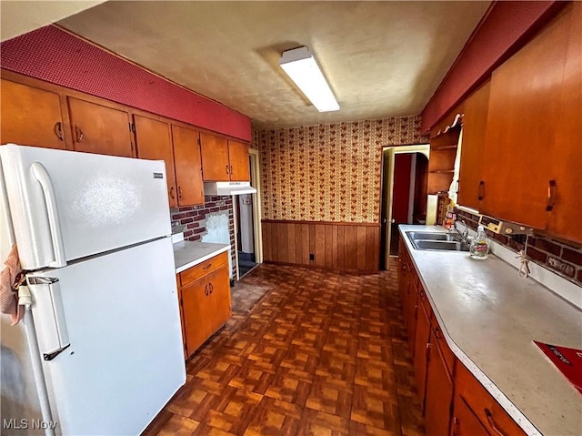 kitchen with white refrigerator, dark parquet floors, wooden walls, and sink