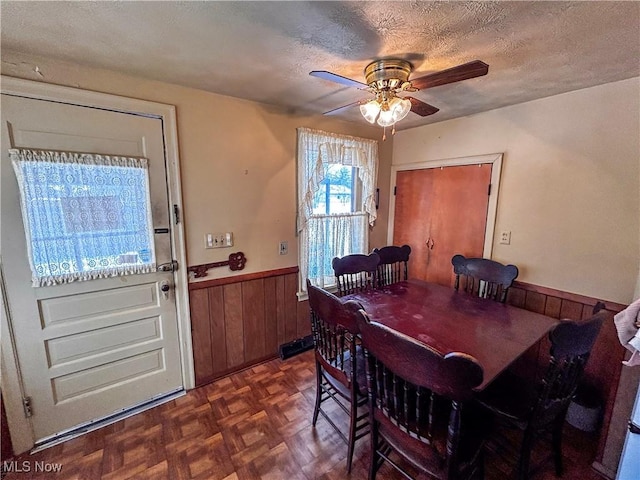 dining area with a textured ceiling, ceiling fan, dark parquet floors, and wooden walls