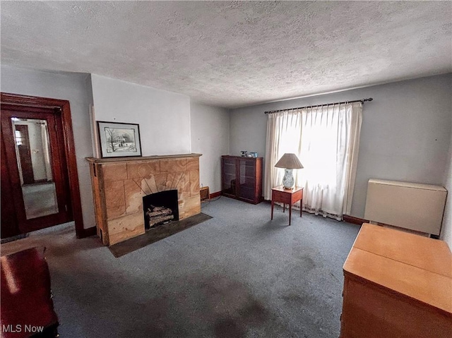 living room with a stone fireplace, a textured ceiling, and dark colored carpet