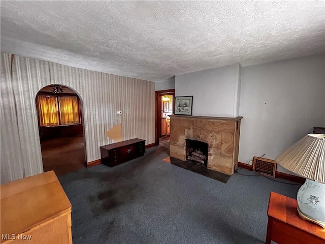 living room featuring a textured ceiling, a fireplace, and dark carpet