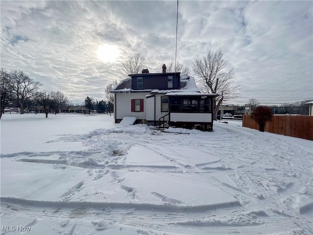 snow covered rear of property featuring a sunroom