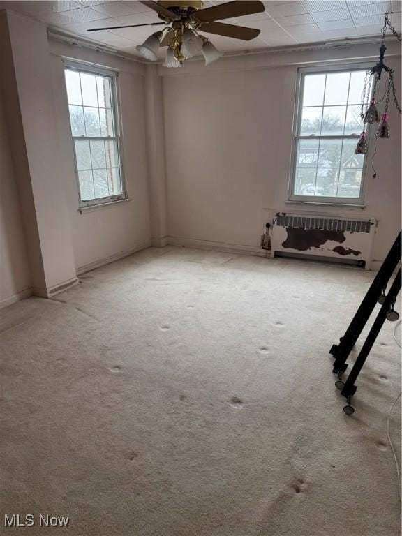 carpeted spare room featuring radiator heating unit, ceiling fan, and plenty of natural light