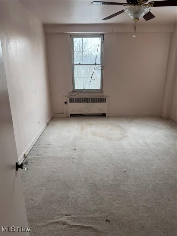 empty room with carpet flooring, baseboards, radiator heating unit, and ceiling fan