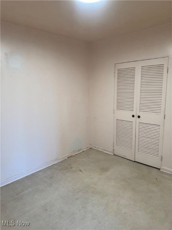 unfurnished bedroom with a closet, concrete flooring, and baseboards