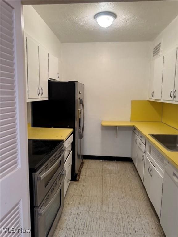 kitchen with a sink, double oven range, a textured ceiling, white cabinets, and light countertops