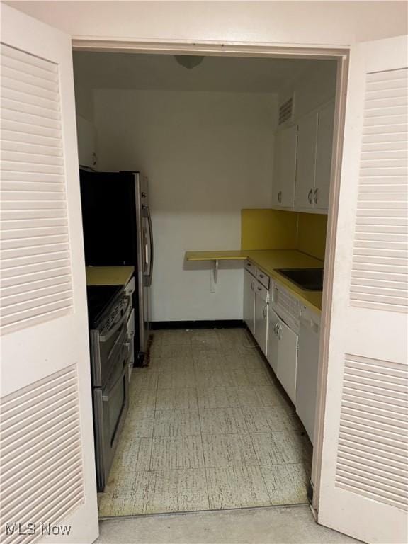 kitchen with visible vents, baseboards, range with two ovens, white cabinetry, and a sink