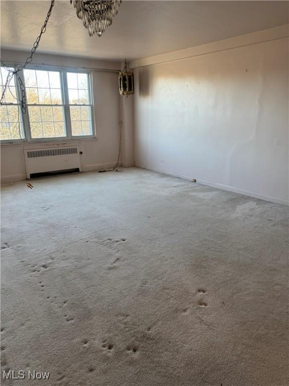 carpeted spare room featuring radiator and baseboards