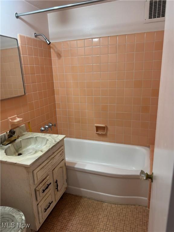 full bathroom with tile patterned floors, visible vents, tile walls, bathing tub / shower combination, and vanity