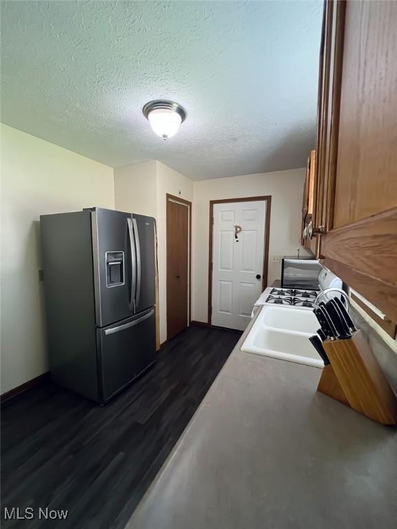 kitchen with baseboards, a sink, dark wood-type flooring, stainless steel refrigerator with ice dispenser, and a textured ceiling