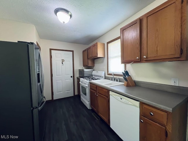 kitchen with dark wood-style floors, brown cabinetry, white appliances, a textured ceiling, and a sink