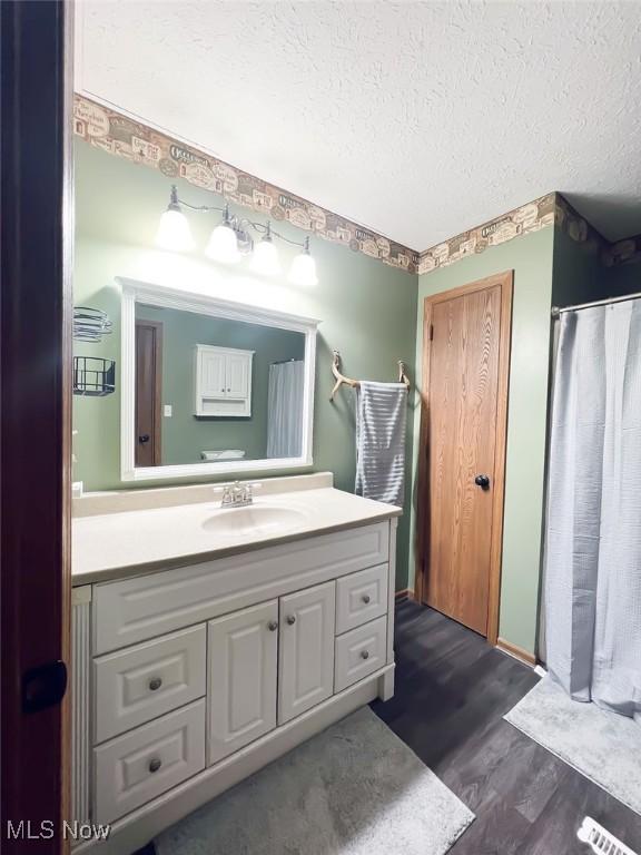 full bath with a shower with curtain, a textured ceiling, wood finished floors, and vanity