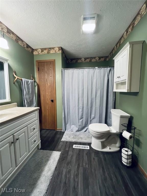 full bath with toilet, wood finished floors, vanity, and a textured ceiling