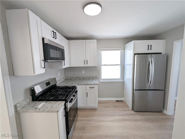 kitchen with light hardwood / wood-style floors, light stone countertops, white cabinetry, and stainless steel appliances