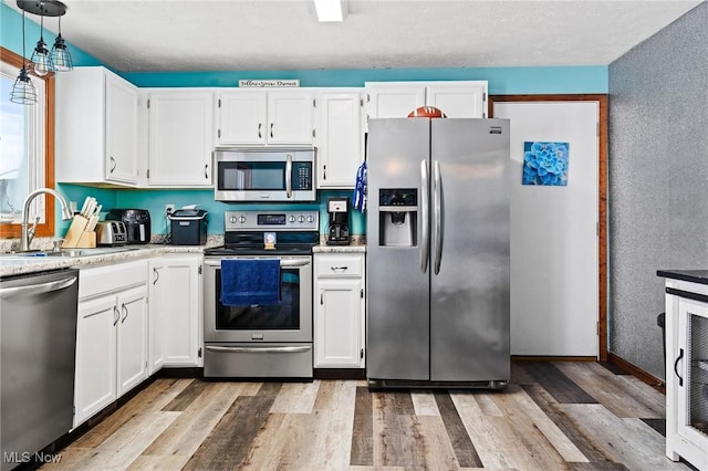 kitchen with decorative light fixtures, light hardwood / wood-style floors, white cabinets, and stainless steel appliances