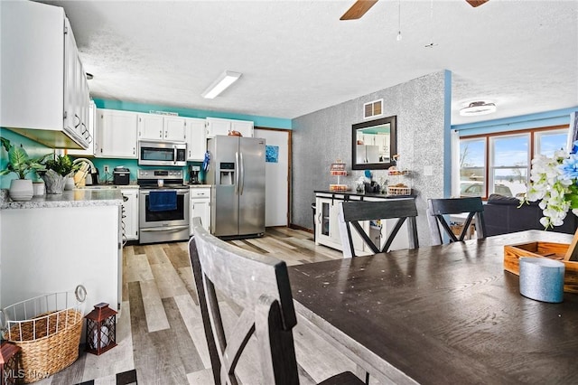 kitchen featuring a textured ceiling, white cabinetry, stainless steel appliances, sink, and light hardwood / wood-style flooring