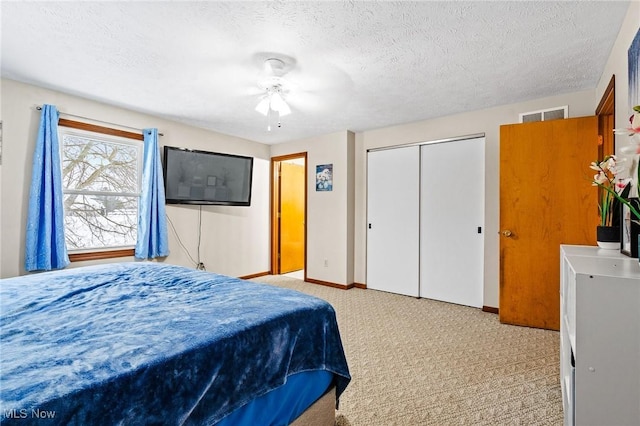 bedroom with a textured ceiling, ceiling fan, a closet, and light colored carpet