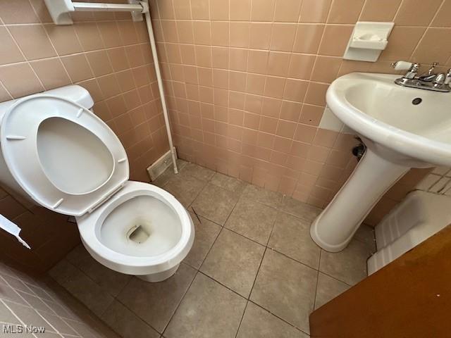 bathroom featuring toilet, tile walls, and tile patterned flooring