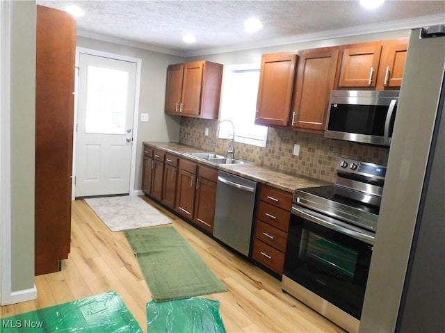 kitchen with appliances with stainless steel finishes, decorative backsplash, crown molding, light hardwood / wood-style flooring, and sink