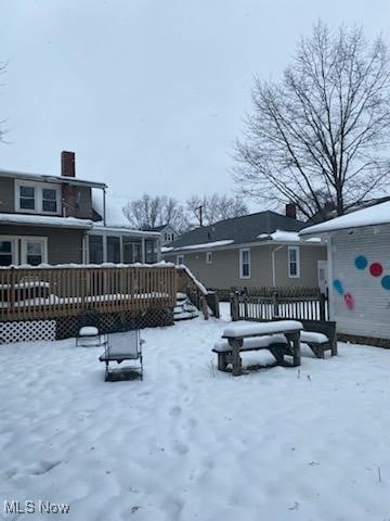 snow covered back of property featuring a wooden deck and a sunroom