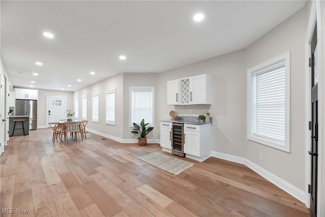 kitchen with a healthy amount of sunlight, beverage cooler, white cabinetry, and stainless steel refrigerator