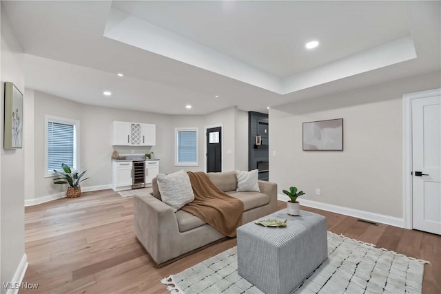 living room with light wood-type flooring, beverage cooler, a raised ceiling, and bar