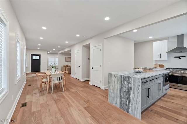 kitchen featuring wall chimney range hood, a center island, white cabinetry, light stone countertops, and high end stainless steel range