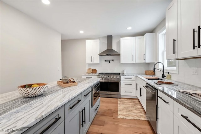 kitchen with wall chimney range hood, white cabinets, and appliances with stainless steel finishes