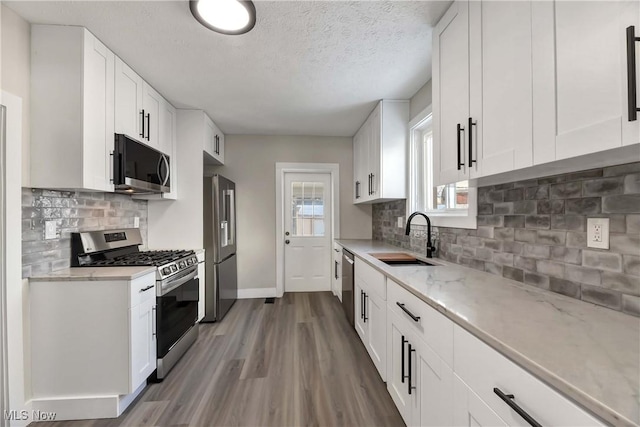 kitchen featuring sink, light stone counters, stainless steel appliances, and white cabinetry