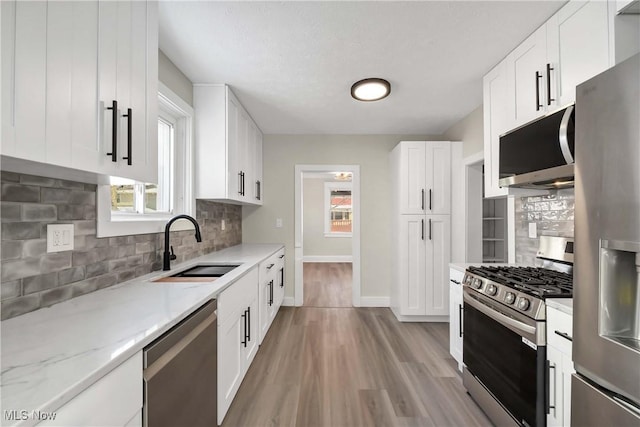 kitchen with decorative backsplash, sink, light stone countertops, appliances with stainless steel finishes, and white cabinets