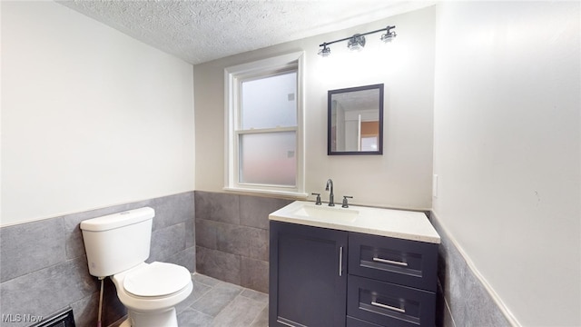 bathroom featuring a textured ceiling, tile patterned flooring, vanity, tile walls, and toilet