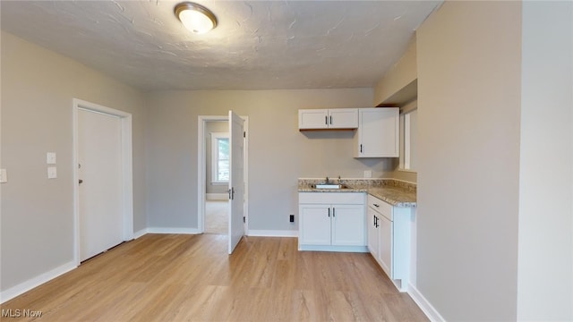 kitchen with light wood-type flooring, sink, and white cabinetry