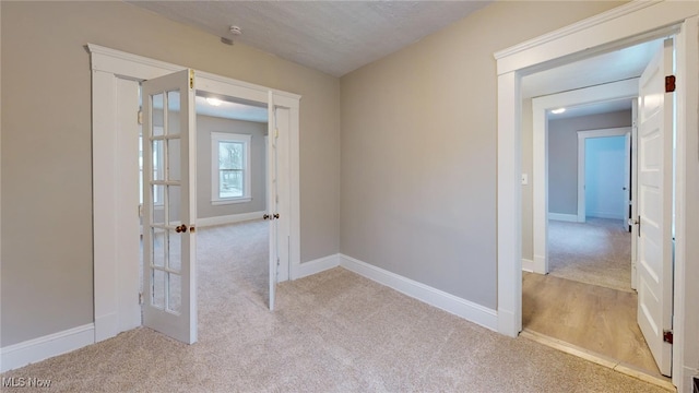 hallway with light carpet, french doors, and a textured ceiling