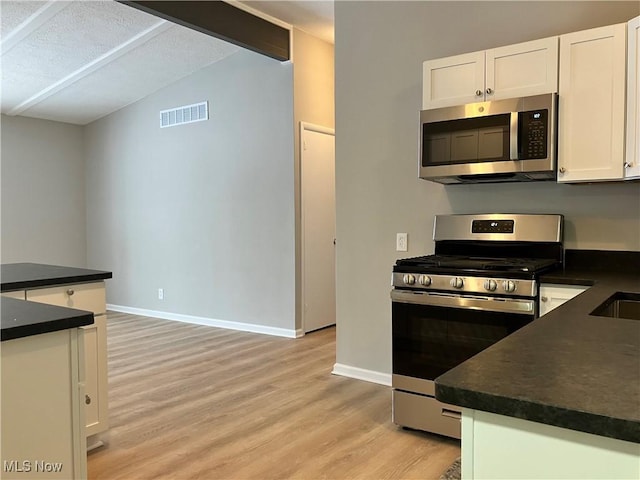 kitchen with a textured ceiling, white cabinets, stainless steel appliances, vaulted ceiling, and light hardwood / wood-style flooring