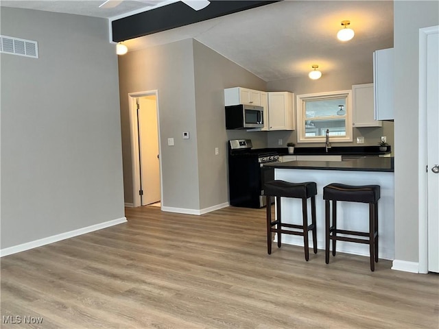 kitchen with white cabinetry, light hardwood / wood-style floors, stainless steel appliances, a kitchen breakfast bar, and lofted ceiling