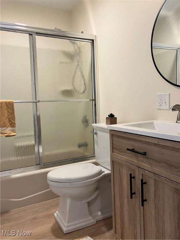 full bathroom featuring toilet, enclosed tub / shower combo, hardwood / wood-style flooring, and vanity