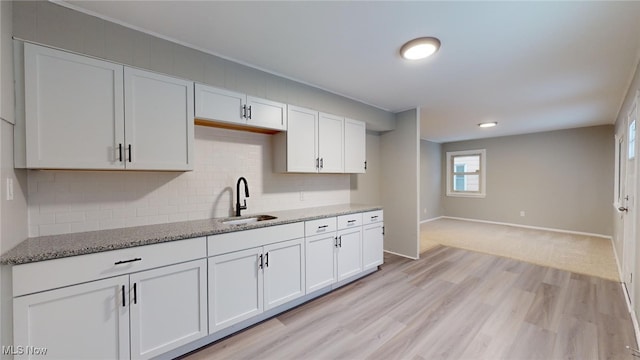 kitchen with white cabinetry, light hardwood / wood-style floors, light stone counters, and sink