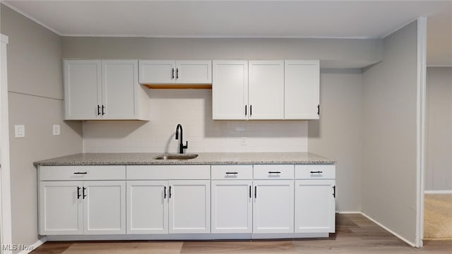 kitchen featuring decorative backsplash, sink, white cabinetry, and light wood-type flooring