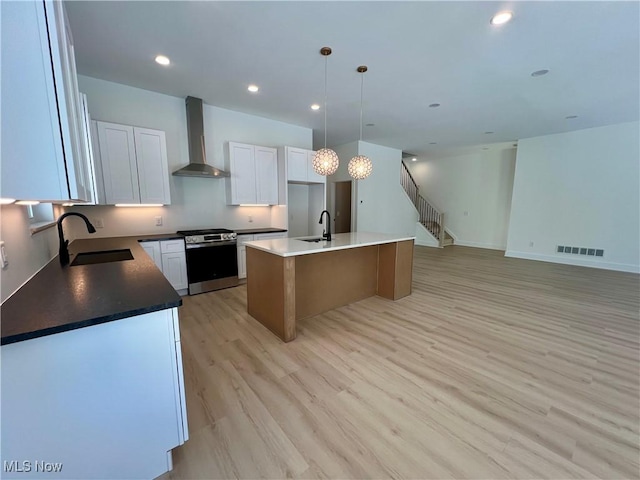 kitchen with stainless steel gas range oven, a kitchen island, wall chimney exhaust hood, white cabinets, and sink