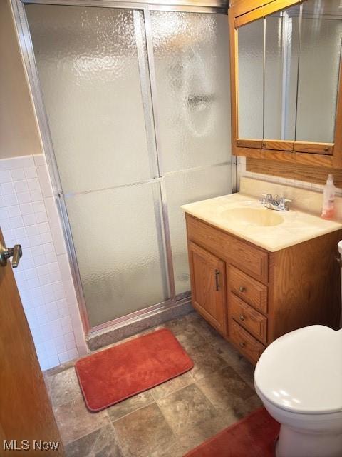 bathroom featuring toilet, a shower stall, tile walls, and vanity