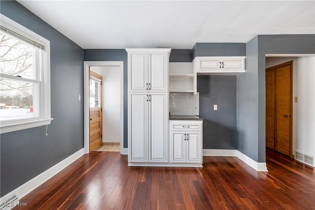 kitchen with dark wood-type flooring, white cabinets, and backsplash