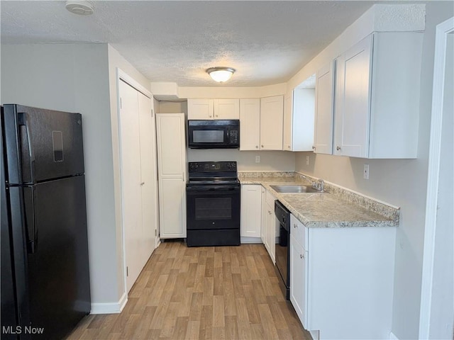 kitchen featuring a textured ceiling, black appliances, white cabinetry, sink, and light hardwood / wood-style flooring