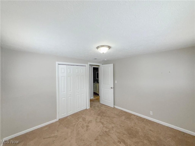 unfurnished bedroom with a textured ceiling, a closet, and light colored carpet