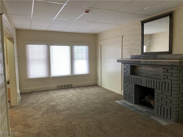 unfurnished living room with a drop ceiling, a brick fireplace, and carpet flooring