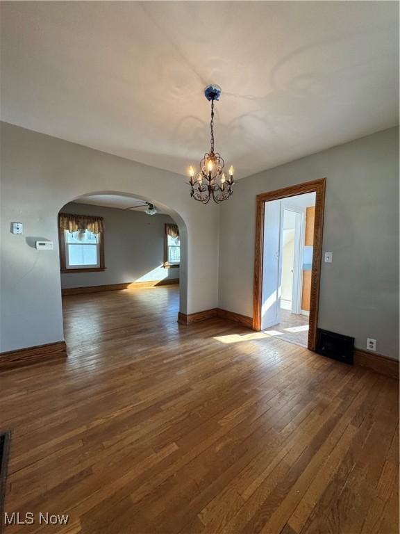 unfurnished room with ceiling fan with notable chandelier and dark hardwood / wood-style flooring