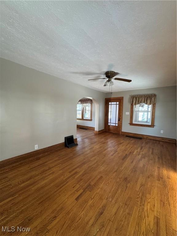 unfurnished living room with a healthy amount of sunlight, dark wood-type flooring, and a textured ceiling